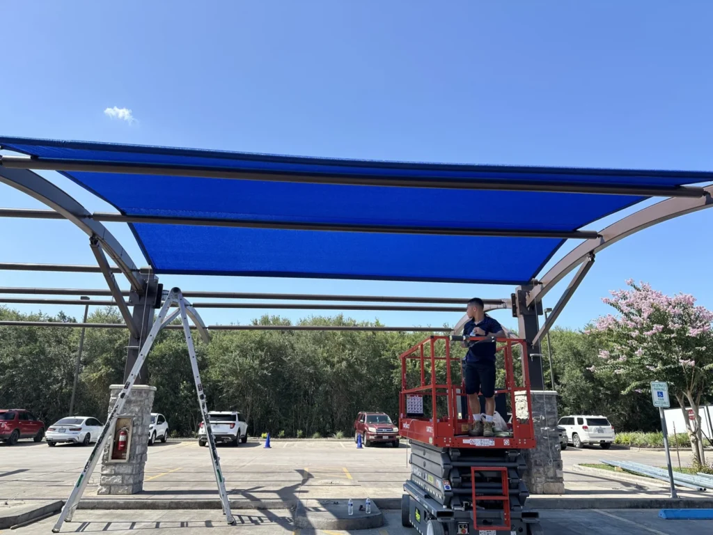 Crew installing blue shade fabric from a scissor lift